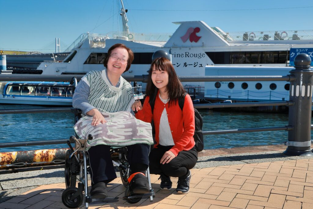 車椅子に座ったお母さんと娘さんの海の前での笑顔な写真